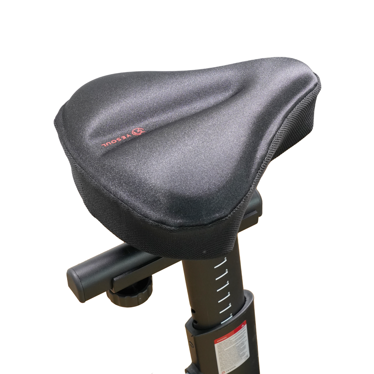 Side view of the YESOUL wide bike seat cover installed on an indoor exercise bike, showing the adjustable seat post and padded saddle cushion.